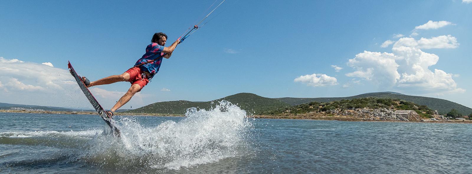spot de kitesurf à Urla en Turquie avec un kiteur en action sur l'eau, un beau paysage avec des colines derrière et un ciel bleu