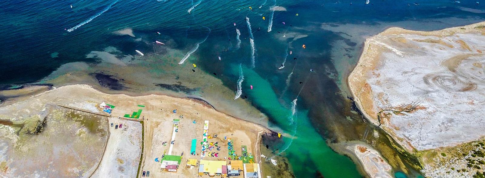 Spot de kitesurf et de l'hôtel Urla Surf House en Turquie avec des kiteurs, des logements, la plage, une eau bleu claire et une vue de drône