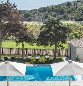 Terrasse ensoleillée du château Hospitalet avec une piscine et son eau bleu claire, des transats, des parasols, en pleine nature avec plein de verdures et les vignes de vin