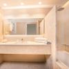 Salle de bain en marbre beige, avec un lavabo blanc, un grand mirroir et douche baignoire