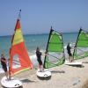 Cours de windsurf au bord de la plage, sur un sable blanc et face à une eau turquoise 