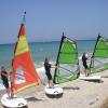 Cours de windsurf au bord de la plage, sur un sable blanc et face à une eau turquoise
