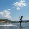 Kitesurfeur en train de sauter sur le spot de Urla en Turquie avec la main dans l'eau entouré de ciel bleu et colines