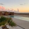 Piscine de l'hôtel ecolodge la Tour d'Eole avec un palmier, des transats, une vue sur l'océan et la ville de Dakhla ainsi qu'un coucher de soleil rose