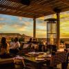 Apéro dans le restaurant et bar en bois de l'hôtel ecolodge de la Tour d'Eole en fin de journée avec un coucher de soleil, des clients qui discutent et des tables prêtes pour dîner