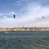Spot de kitesurf flat à la Tour d'Eole derrière les dunes de sable du désert du Sahara avec un ciel bleu et des kitesurfeurs en pleine session