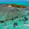 Deux windsurfeurs en action sur l'eau truquoise et transparente du lagon de Madagascar avec une petite île au loin avec du sable blanc, des coraux et de la végétation