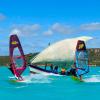 Deux windsurfeurs entrain de naviguer sur le spot flat avec une eau turquoise et un bateau voilier qui les suit derrière